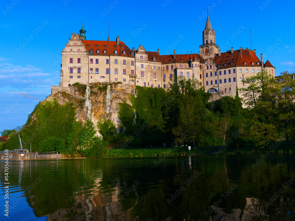 Obraz premium Historic castle perched on rocky cliff with reflection in calm water at sunset