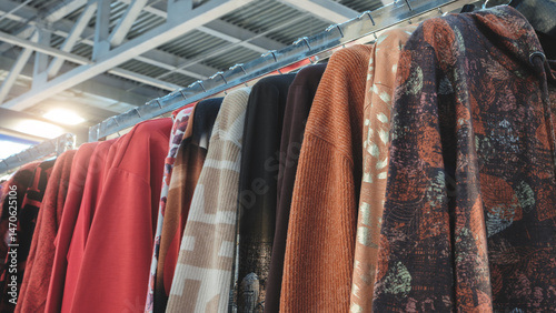 A row of clothes hanging on a rack, including a red shirt with a black stripe and a brown shirt with a gold leaf design