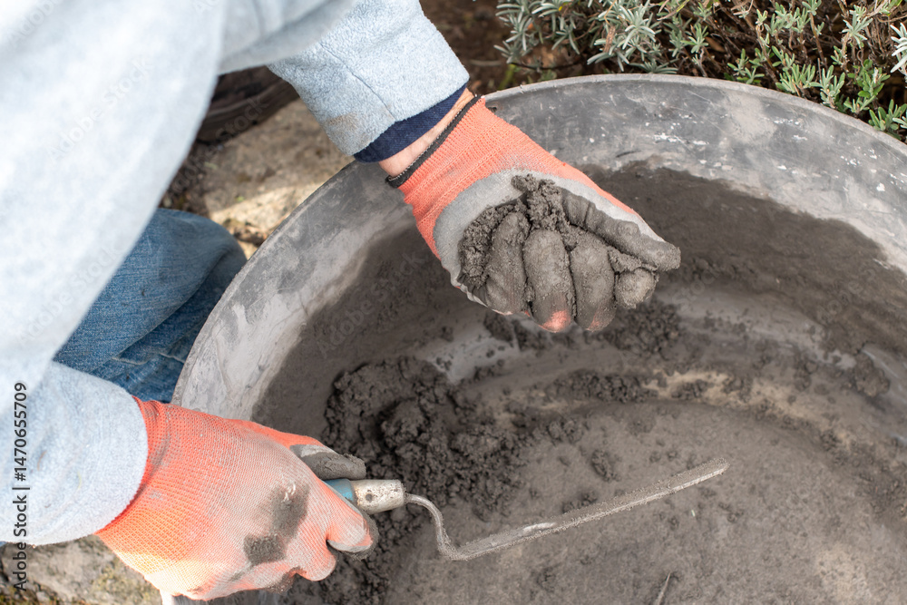 Obraz premium Construction worker wearing gloves mixes cement mortar in a bricklaying basin, ensuring the optimum texture for a strong bond