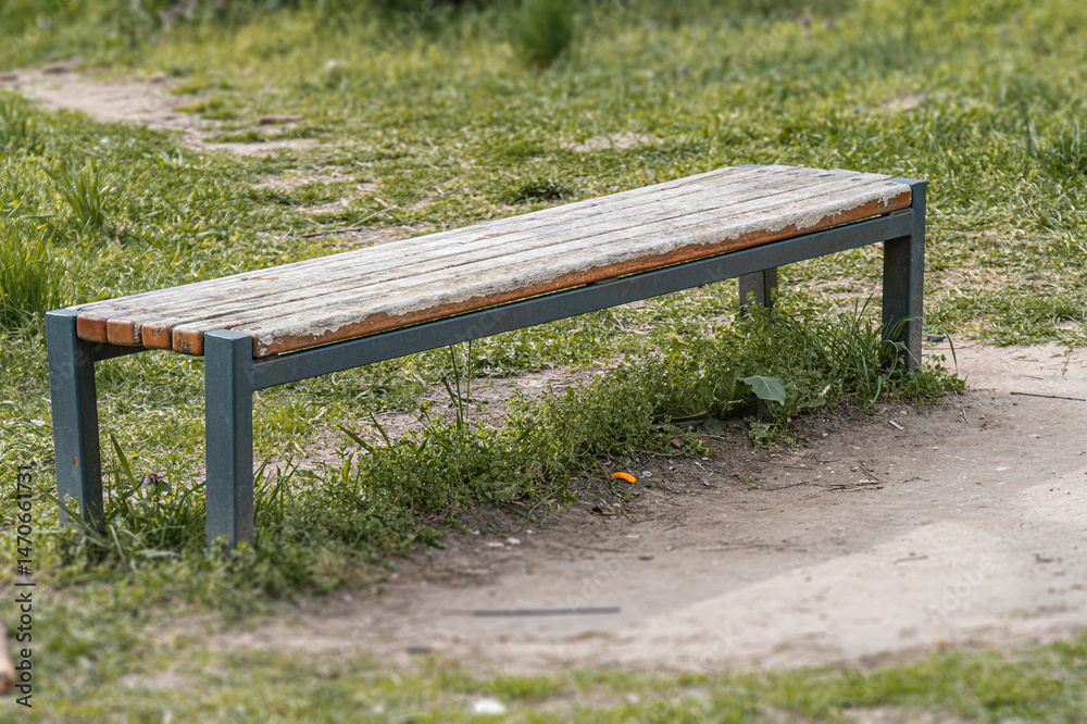 Fototapeta premium An unoccupied, weathered wooden bench with metal legs in a natural outdoor setting The ground is uneven, and the lighting suggests an overcast day Muted earth tones dominate the scene