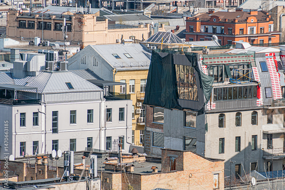 Fototapeta premium Cityscape with various buildings, overhanging canopy structure under construction, scaffolding and material coverings, urban environment, muted earthy tones, overcast sky, rooftops, pitched roofs, mu