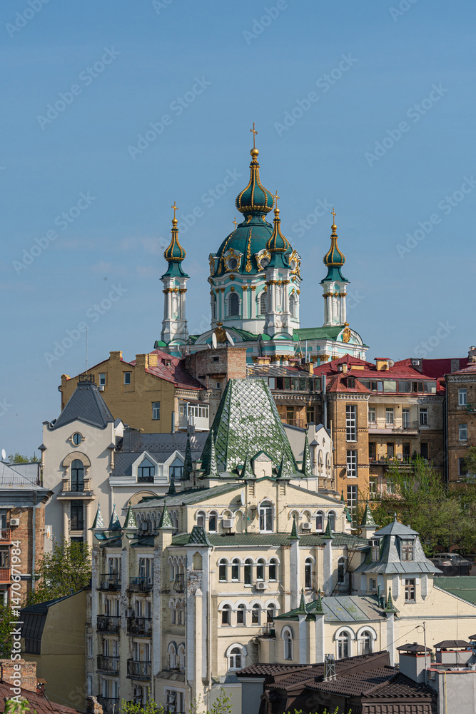 Fototapeta premium A captivating image of an Eastern Orthodox church, showcasing multiple onion-domes, standing as a central landmark in a densely built-up urban area The structure is richly a - Kyiv, Ukraine 06-11-2024