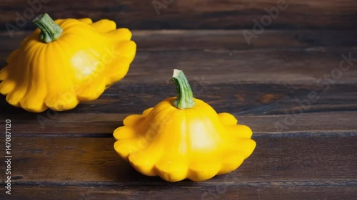 Two bright yellow pattypan squash on dark wooden surface