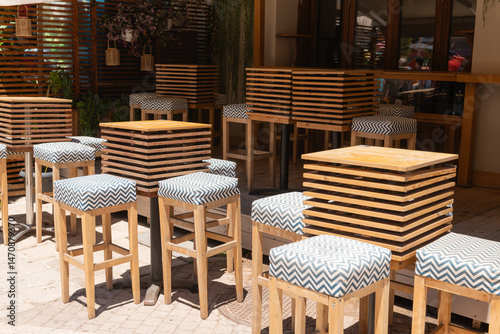 Modern Bar Terrace with High Stools. Stylish outdoor bar area with wooden high tables and patterned stools along a sunny Zakynthos street.