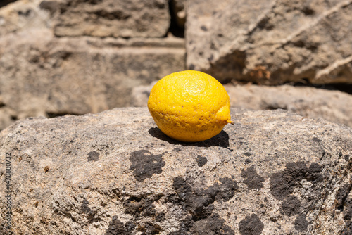 Lemon on Sunlit Stone Surface. Single ripe lemon resting on a weathered stone in Zakynthos, Greece, bathed in warm Mediterranean sunlight.