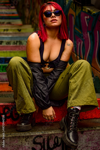 Young woman with red hair posing in an urban staircase covered with graffiti in Comuna 13, Medellín
