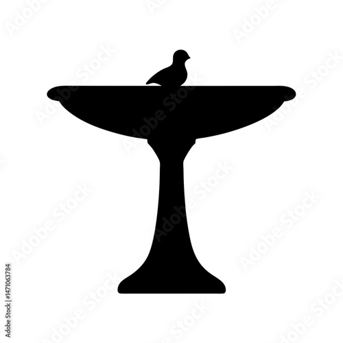Silhouette of a bird perched on a classic bird bath fountain