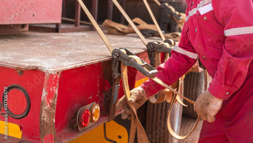 Canvas Print Action of a worker is tightening latching strap belt to secure the load object on trailer truck
