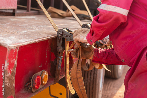 Action of a worker is tightening latching strap belt to secure the load object on trailer truck. Transportation working scene, selective focus.	