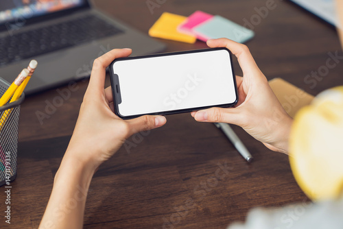 Hand holding smartphone with a blank screen on table, for putting advertising to promote.