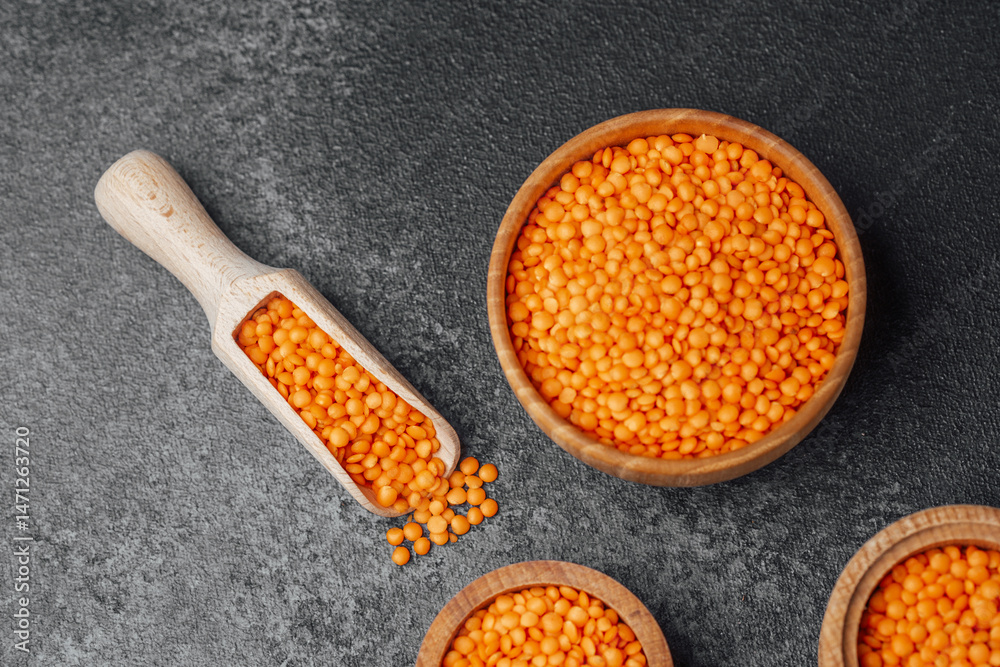 Vibrant orange lentils displayed in wooden bowls on a dark surface