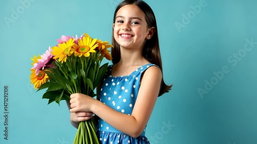 A cute girl in a blue dress with white polka dots holds a bouquet of flowers in her hands and smiles