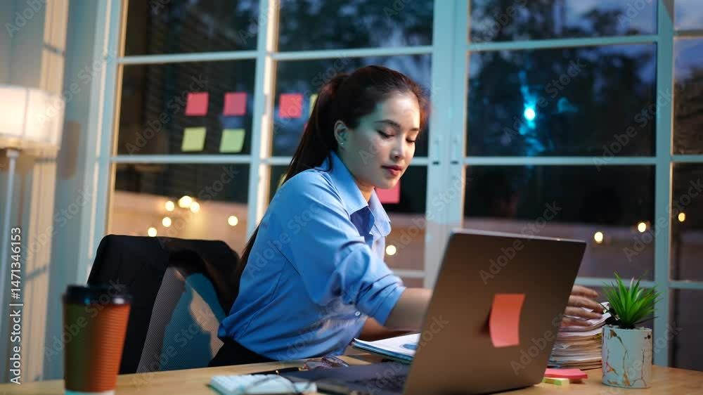 An ambitious Asian businesswoman works late at her desk, focused on sales, planning, and analysis under tight deadlines in a modern office. An ambitious Asian businesswoman works late at her desk, focused on sales, planning, and analysis under tight deadlines in a modern office.