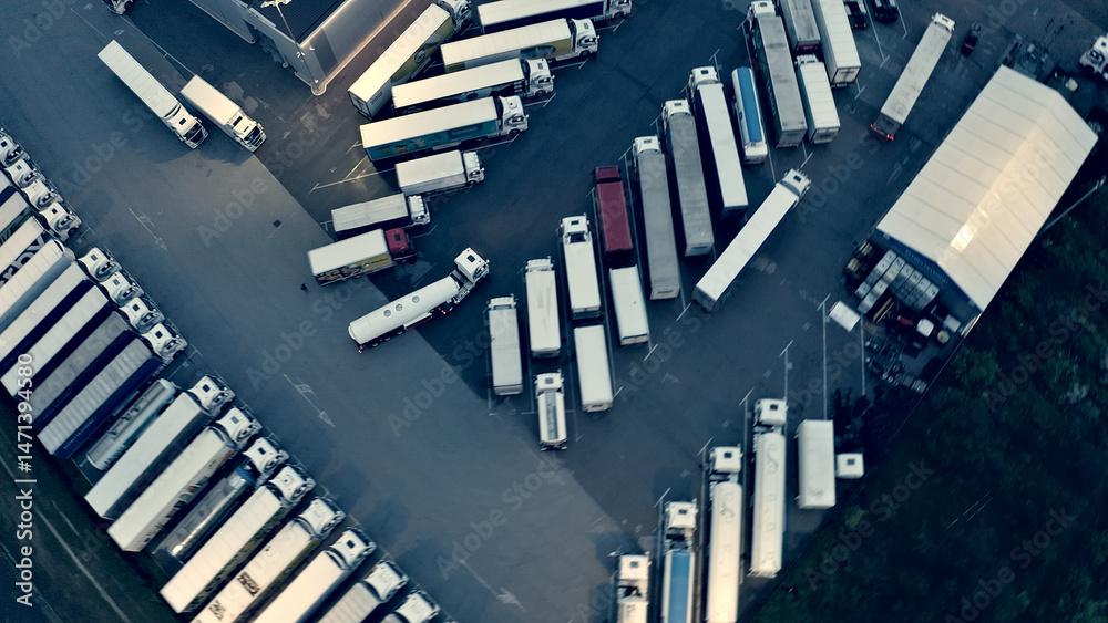 Obraz premium Aerial view of a bustling parking lot filled with rows of trucks and cargo, highlighting transportation and logistics operations.