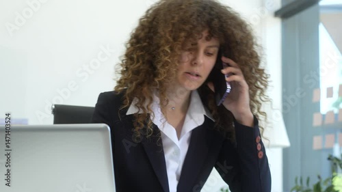 Russian businesswoman with voluminous curly hair intently writes in a notebook at her modern desk, bathed in soft light, embodying professionalism and concentration. She could  Business Consultant.