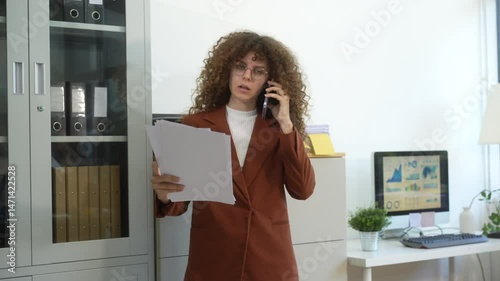 Russian businesswoman with voluminous curly hair intently writes in a notebook at her modern desk, bathed in soft light, embodying professionalism and concentration. She could  Business Consultant.