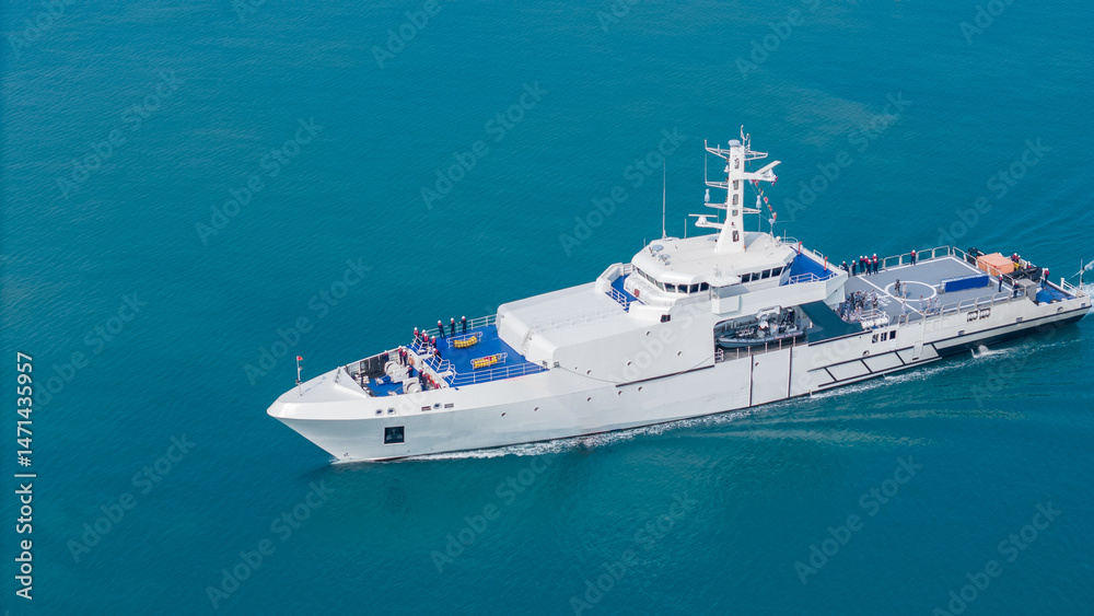 Naklejka premium Aerial view of a modern patrol vessel sailing on calm turquoise sea, equipped with radar, deck equipment, and a helipad. Concept of maritime security, naval operations, and coast guard missions.