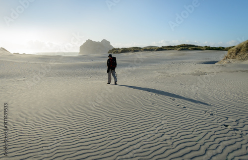 Obraz na płótnie Man walking on the sand beach, casting long shadow on the beach. Wharariki Beach. Golden Bay. South Island. w salonie