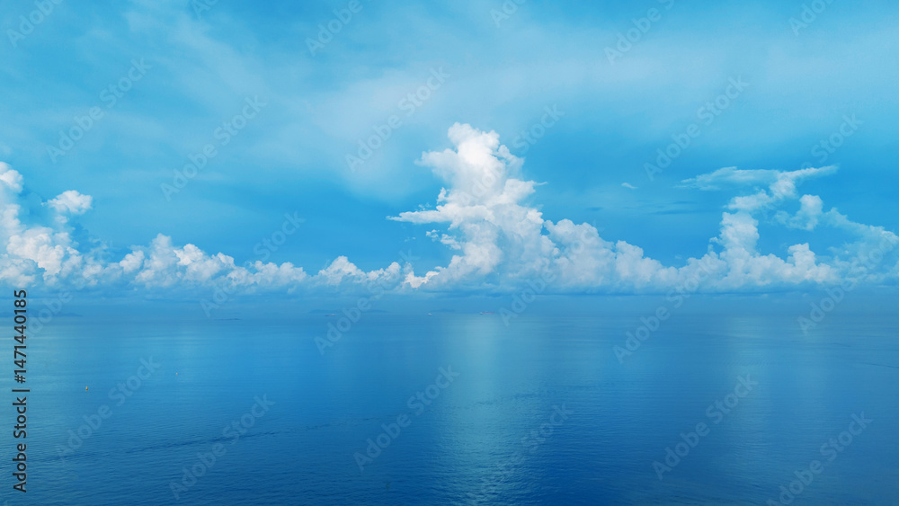 Obraz premium Scenic aerial view of a peaceful seascape with a long pier extending into calm blue waters, surrounded by ships and distant skyline under a vast cloudy sky. Maritime and coastal development concept.