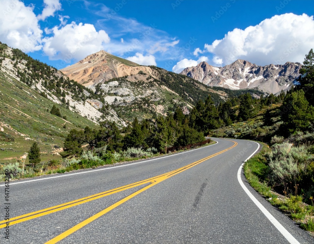 Fototapeta premium Serene Winding Mountain Road Under Blue Sky and White Clouds