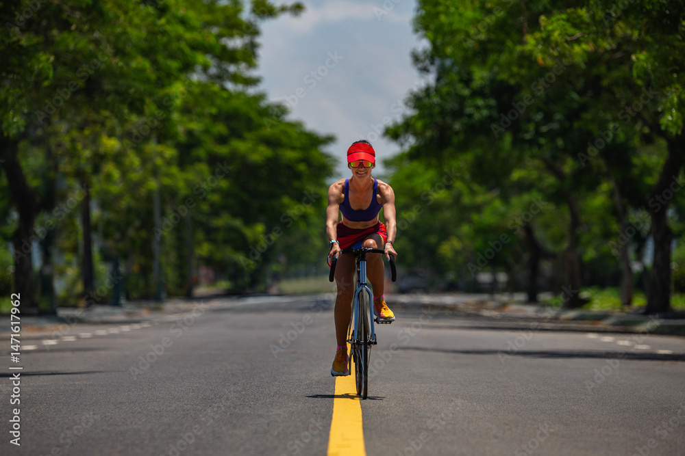 Fototapeta premium Fit woman cycling on empty road in summer, front view..