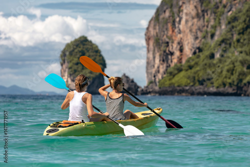 Two girls kayak across turquoise water to limestone island, Phi-Phi islands, Krabi province, Thailand
