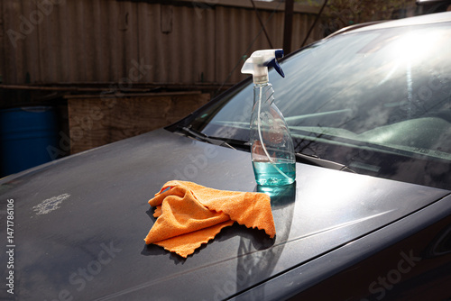 Household chore: car washing supplies, including a spray cleaner and microfiber towel, ready for use on a dirty car.