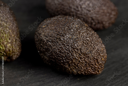 several whole black avocado fruits of small size on a black slate