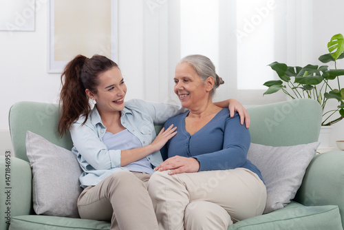 Granddaughter hugs her smiling grandmother with love and joy. Warm and happy family moment at home showing affection, connection, and generational bond between two women in a cozy and peaceful setting