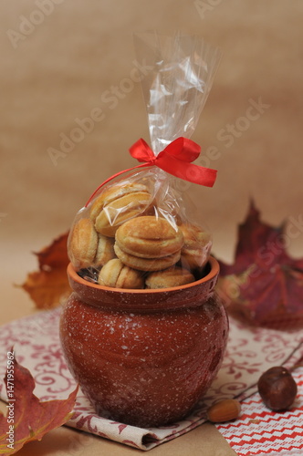 cookies that look like nuts, tied with a bow in a brown ceramic pot. In the background are acorns, maple leaves and a napkin
