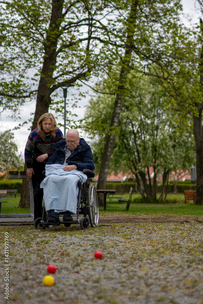 Fototapeta premium adult middle age daughter playing boule with elderly father in wheelchair outside in spring