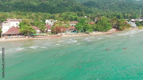 Scenic koh chang island white sand beach with crystal-clear turquoise waters, lush tropical forest backdrop featuring relaxing tourists enjoying serene seaside resort scenery