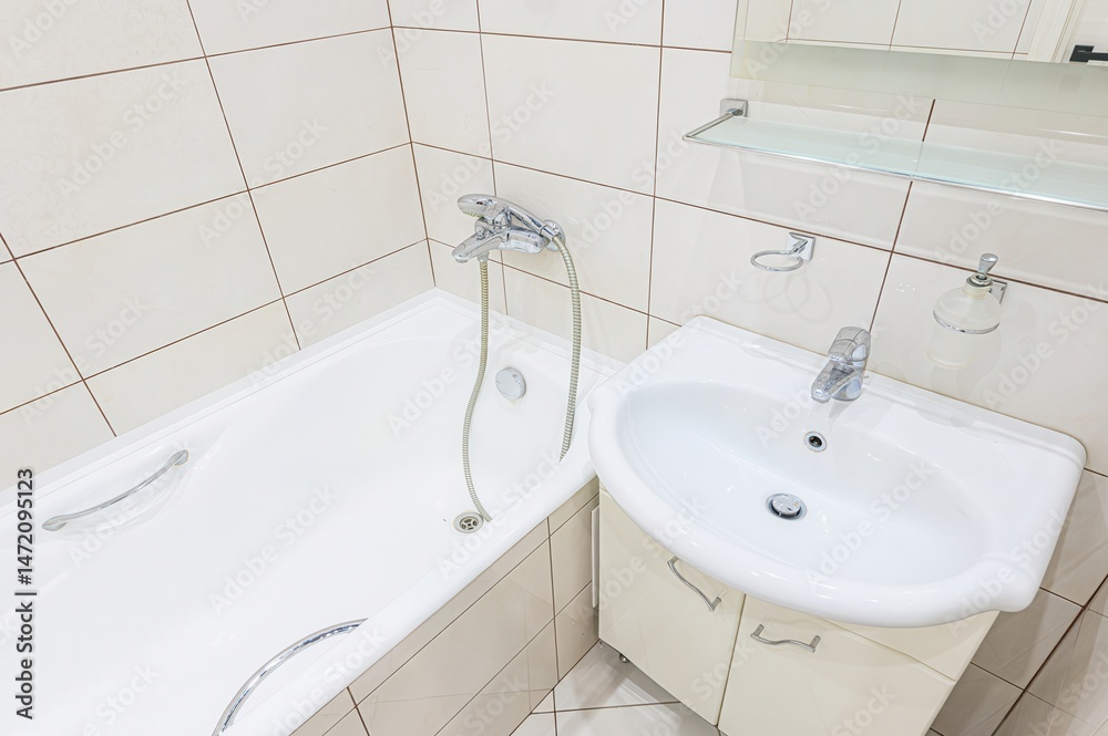 Clean bathroom featuring a white bathtub, sink with cabinet, beige tiles, and chrome fixtures. Minimalist design. Clean bathroom featuring a white bathtub, sink with cabinet, beige tiles, and chrome fixtures. Minimalist design.