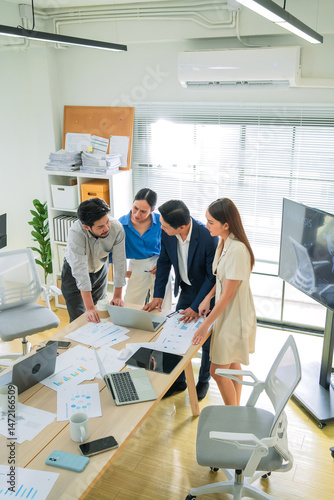 Group of business people reviewing financial charts and laptop insights while standing in office meeting, focused on planning, strategy, and team success
