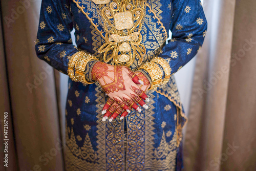 Portrait of a beautiful bride in a traditional Malay dress with henna motifs painted on her hands and decorated with sparkling gold accessories. Riau, Indonesia.