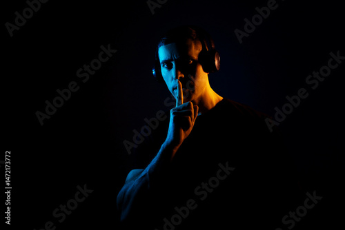Young man with headphones in a dramatic lighting listening to music. Horizontal photo on dark background. Young man in the dark