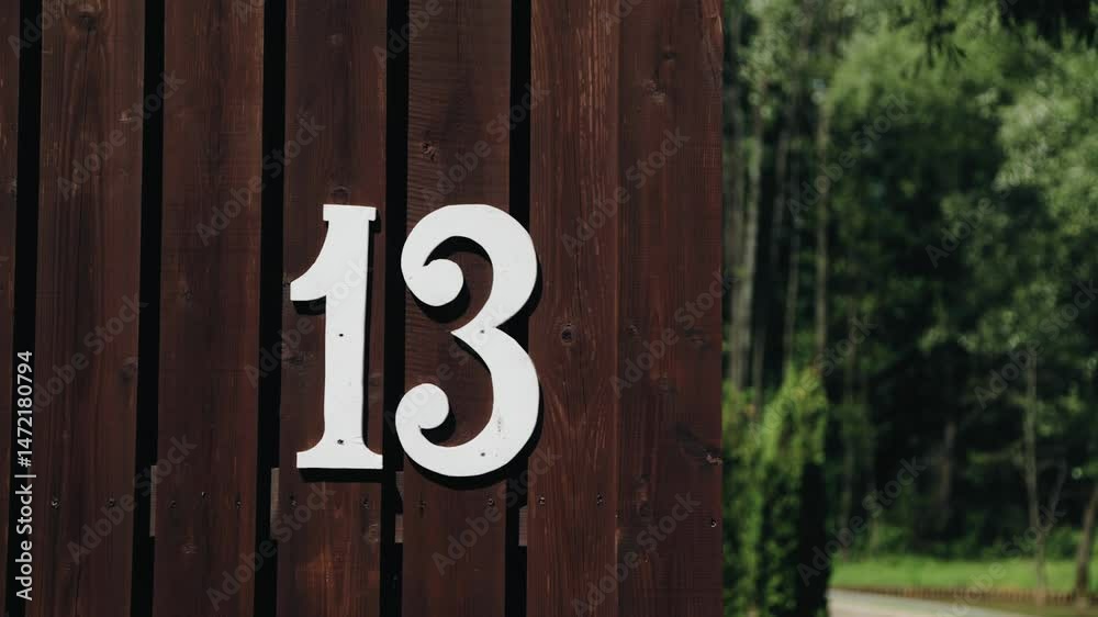 The plate with the number 13 is attached to a wooden fence. The camera captures this number in motion The plate with the number 13 is attached to a wooden fence. The camera captures this number in motion