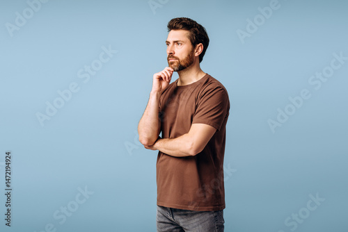 Pensive man touching chin and looking away on blue background