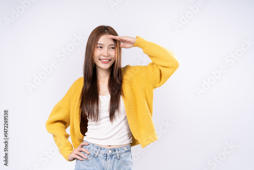 Asian woman in yellow sweater posing looking at something in the distance with her hand and looking interested. Portrait photography on white background.