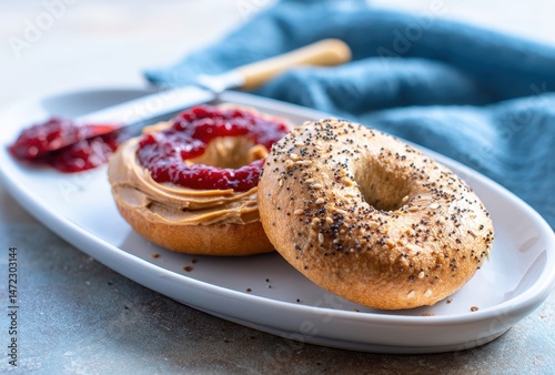 Freshly Baked Bagels with Creamy Peanut Butter and Sweet Raspberry Jam on a Plate with Blue Linen Background, Perfect for Breakfast and Snack Ideas