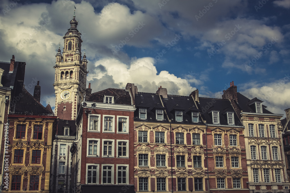 Fototapeta premium Colorful historic facades line the town square in Lille, France. Elegant belfry clock tower and dramatic sky in background.