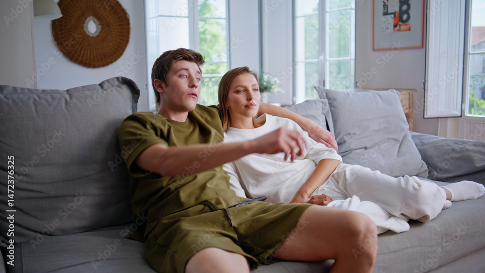 Happy spouses enjoying tv program at couch. Smiling man embracing girlfriend