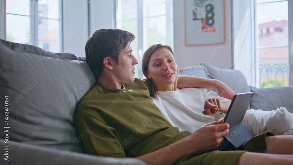 Relaxed pair staring pad computer at home. Loving teenagers shopping online