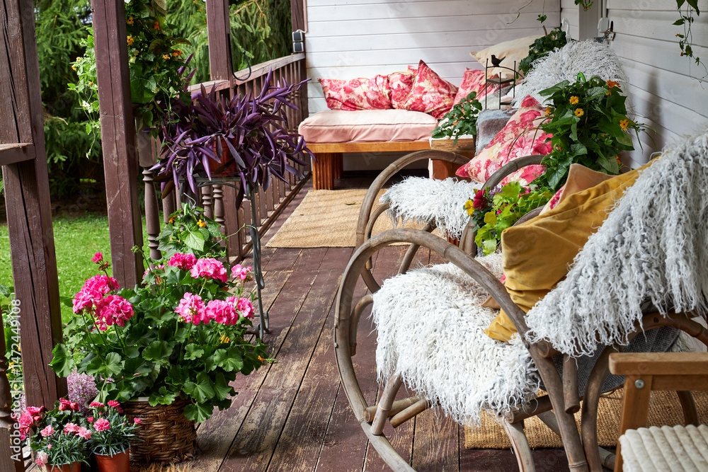 Fototapeta premium View of a modern-style summer veranda interior decorated with bright summer flowers, rattan rocking chairs, and a large pink sofa