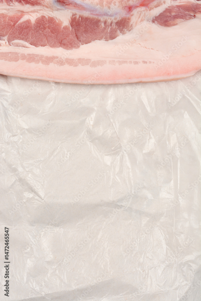 A raw piece of pork belly with distinct layers of meat and fat rests on white butcher paper