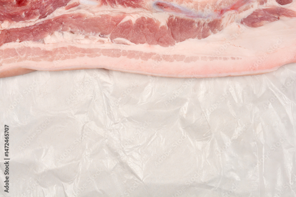A raw piece of pork belly with distinct layers of meat and fat rests on white butcher paper