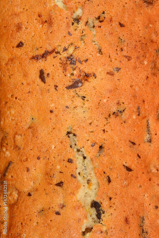 The textured surface of a freshly baked loaf cake with walnuts, raisins, chocolate pieces, and orange zest