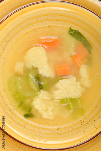 Obraz na płótnie A close-up shows a yellow bowl filled with clear vegetable soup containing semolina dumplings, carrots, and green herbs w salonie