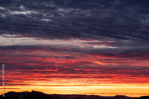 Dramatic sunset with layered clouds over distant horizon, rich in warm and dark hues, conveying serenity, depth and emotional tone for background or inspirational concepts.