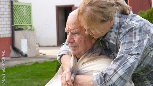 Old woman caring husband, covering him with blanket and embracing him with love. Tender moments affection and support highlight their deep connection couple. Caring dementia patients. Sitting outdoor
